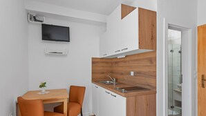 A compact kitchen with a wooden accent wall, a built-in sink, and a TV mounted above the countertop. - Superior Studio Tania 3 (Sveti Filip i Jakov)