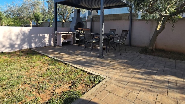 A covered outdoor patio with a grill, seating, and a landscaped garden area. - Studio Apartment Nia (Nin)