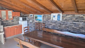 A rustic kitchen with wooden cabinets, a stone backsplash, and a dining area with a wooden table and chairs. - Studio Apartment Nia (Nin)