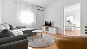 Un salon moderne avec un canapé gris, une petite table blanche et un téléviseur posé sur un meuble blanc.