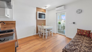 Une pièce de taille modeste comprenant une table à manger, des chaises, un téléviseur fixé sur un panneau en bois, un lit avec une literie à motifs et une horloge au mur.