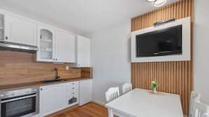 Une cuisine moderne avec des meubles blancs, un four encastré et un four à micro-ondes. On y trouve une table à manger avec des chaises et une petite plante posée sur la table.
