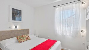 Un lit bien fait, avec une couverture rouge, un coussin à motifs floraux et une tête de lit dotée d’un luminaire.