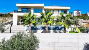 Un bâtiment moderne à deux étages, doté d’une piscine, de palmiers et offrant une vue sur la mer.