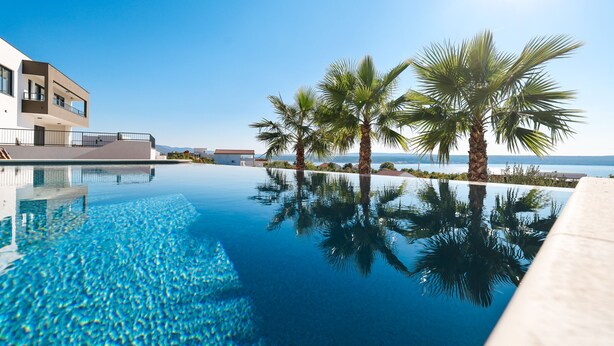 Un hôtel moderne doté d’une piscine, de palmiers et offrant une vue sur la mer.