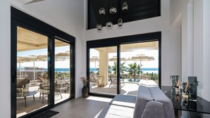 Un vaste espace de vie comprenant un grand canapé, une table basse en verre et une vue sur la terrasse extérieure, agrémentée de parasols et de sièges.