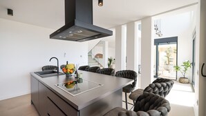 Une cuisine moderne dotée d’un îlot central, de tabourets de bar à assise rembourrée de couleur sombre et d’une hotte noire au design épuré.