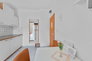 A compact kitchen with white cabinets, a wooden countertop, and a dining area with a table and chairs. - Superior Studio Tania 5 (Sveti Filip i Jakov)