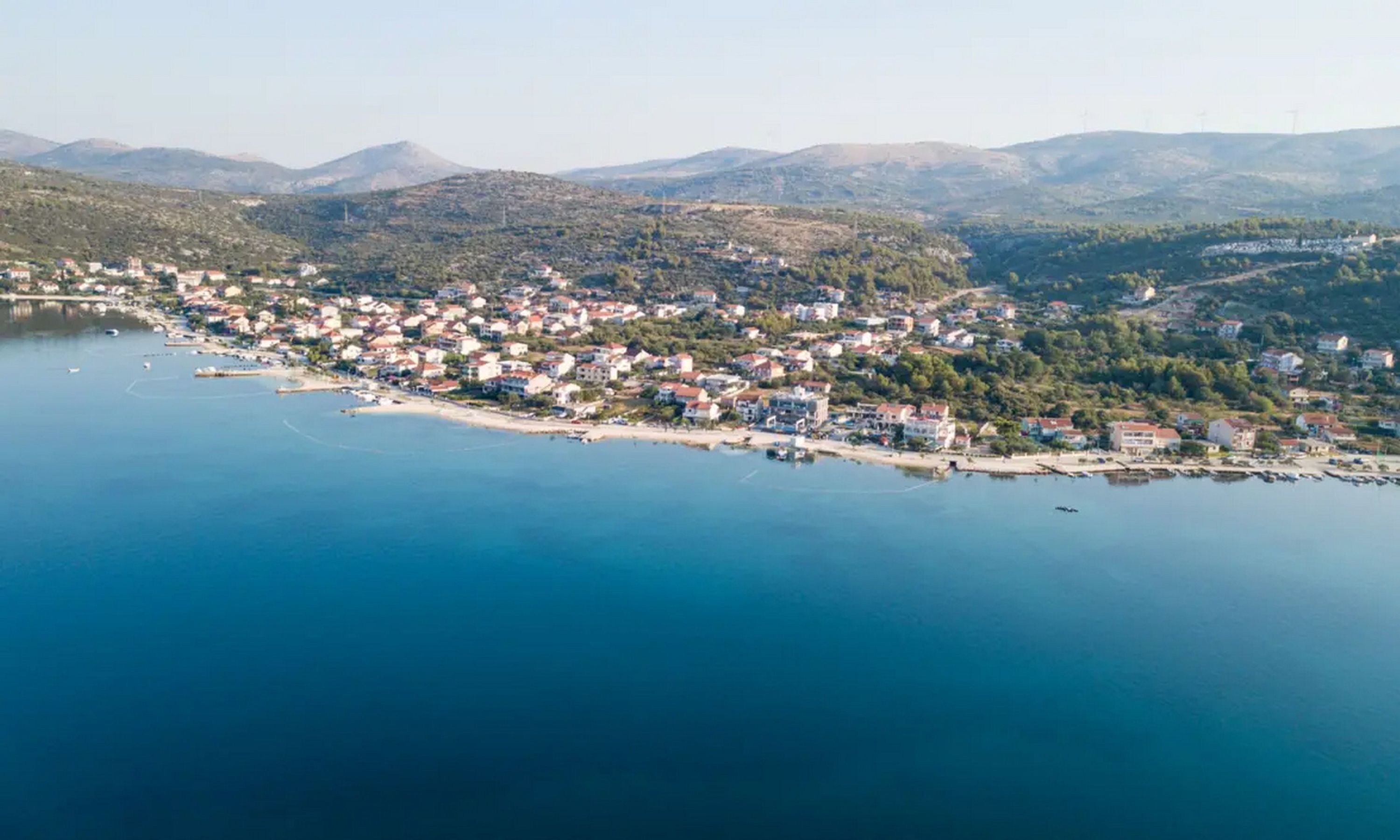 Vista aérea de un pueblo costero con un puerto deportivo, rodeado de colinas y montañas.