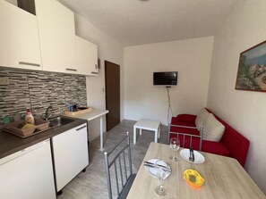 Une cuisine moderne avec des meubles blancs, un pare-feu en carrelage et un évier. On y trouve également un coin repas avec une table en bois, un canapé rouge et un téléviseur fixé au mur.