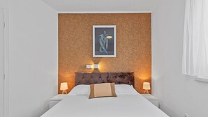 Ett hotellrum med en säng, två sänglampor, en sänggavel och ett inramat konstverk på väggen.