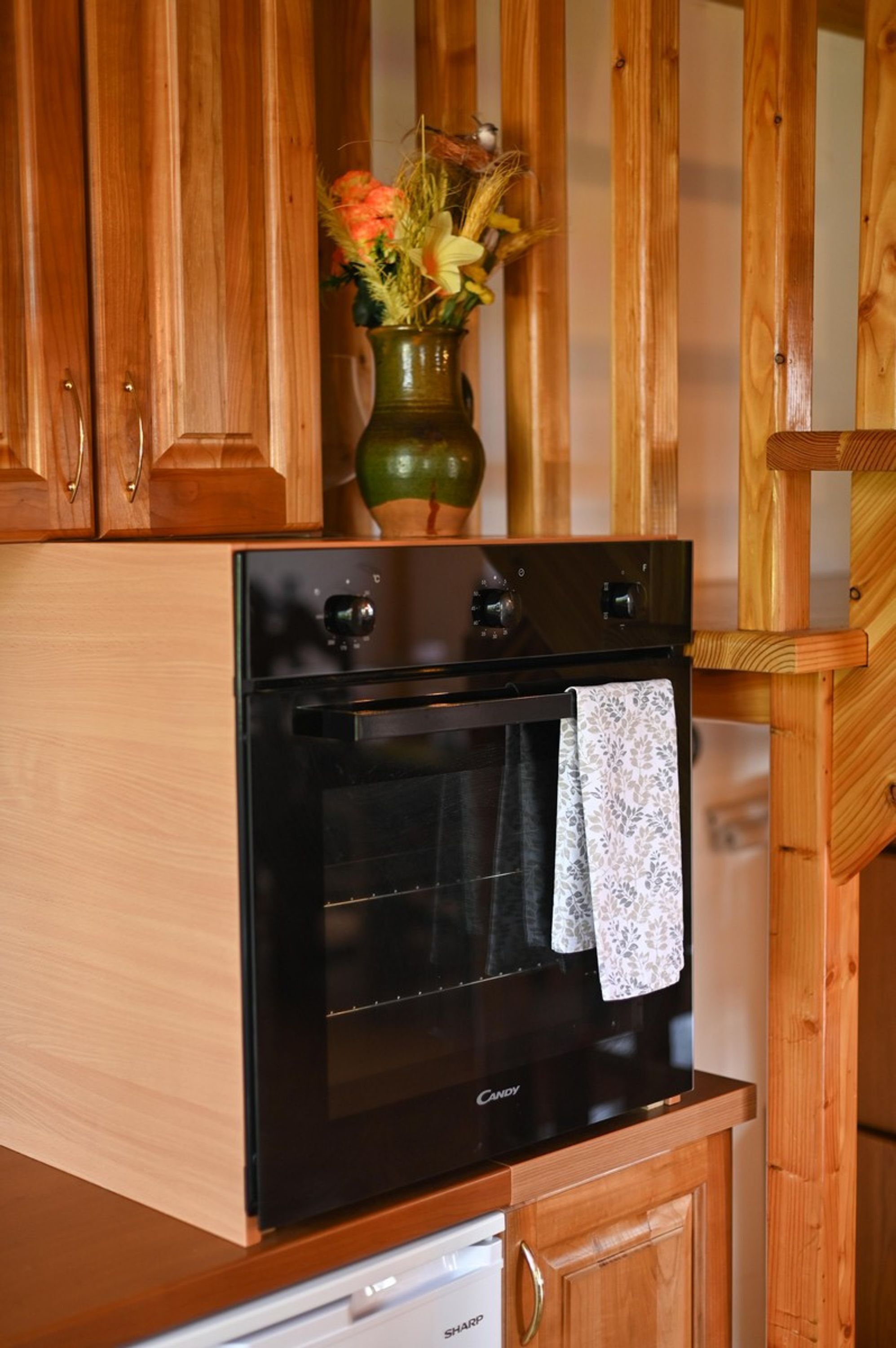 A kitchen with wooden cabinets, a black oven, and a vase with flowers.