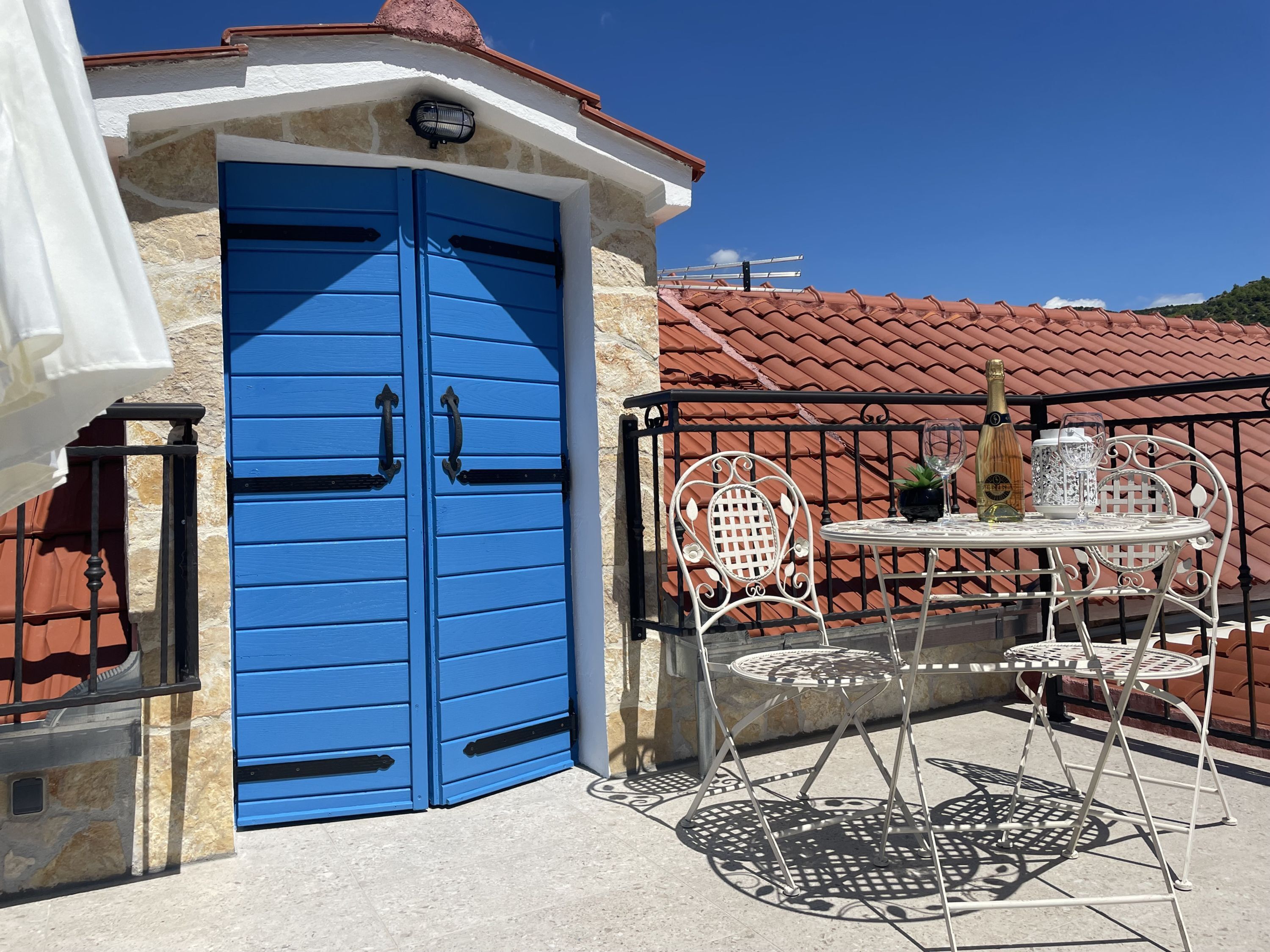 A blue door with black handles, a white table with two chairs, and a bottle of champagne on the table.