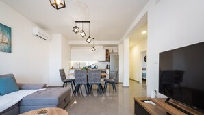 A modern living room with a sofa, a dining table with chairs, a TV, and a kitchen in the background. - Apartment Vista Mare 2 With Heated Pool (Sveti Filip i Jakov)