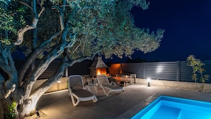An outdoor pool area with lounge chairs, a fire feature, and a tree. - Apartment Vista Mare 2 With Heated Pool (Sveti Filip i Jakov)