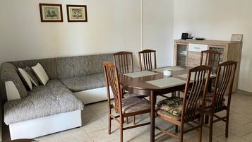 A living room with a grey sofa, wooden dining table with chairs, and a cabinet.