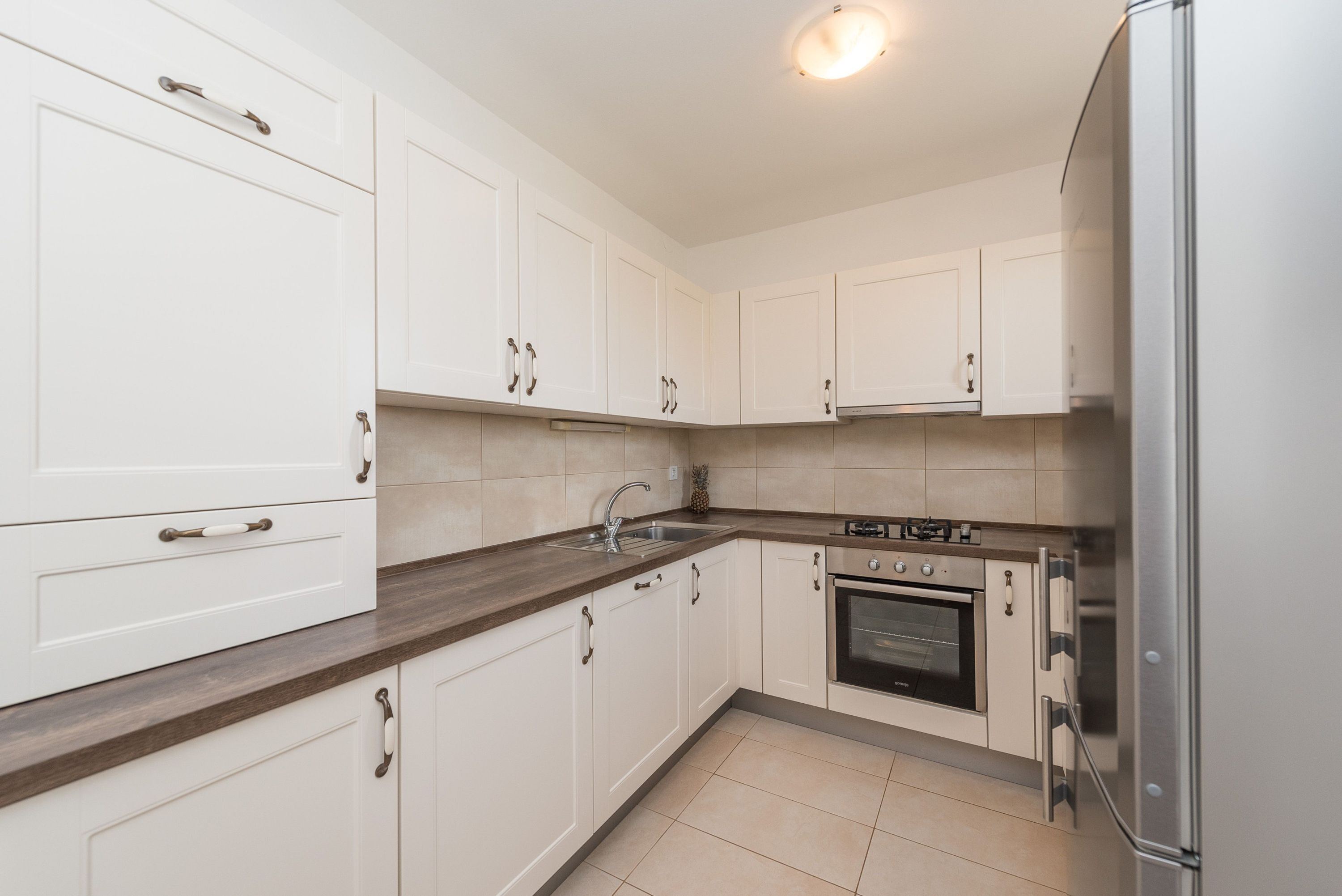 A modern kitchen with white cabinets, a stainless steel refrigerator, and a built-in oven.