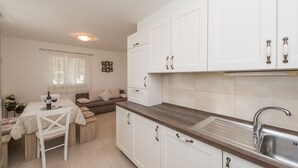 A compact kitchen with white cabinets, a stainless steel sink, and a dining area with a table set for two. - Apartment Brevilacqua (Privlaka)