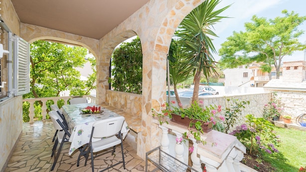 A covered outdoor dining area with stone arches, a table set for two, and potted plants. - Apartment Brevilacqua (Privlaka)