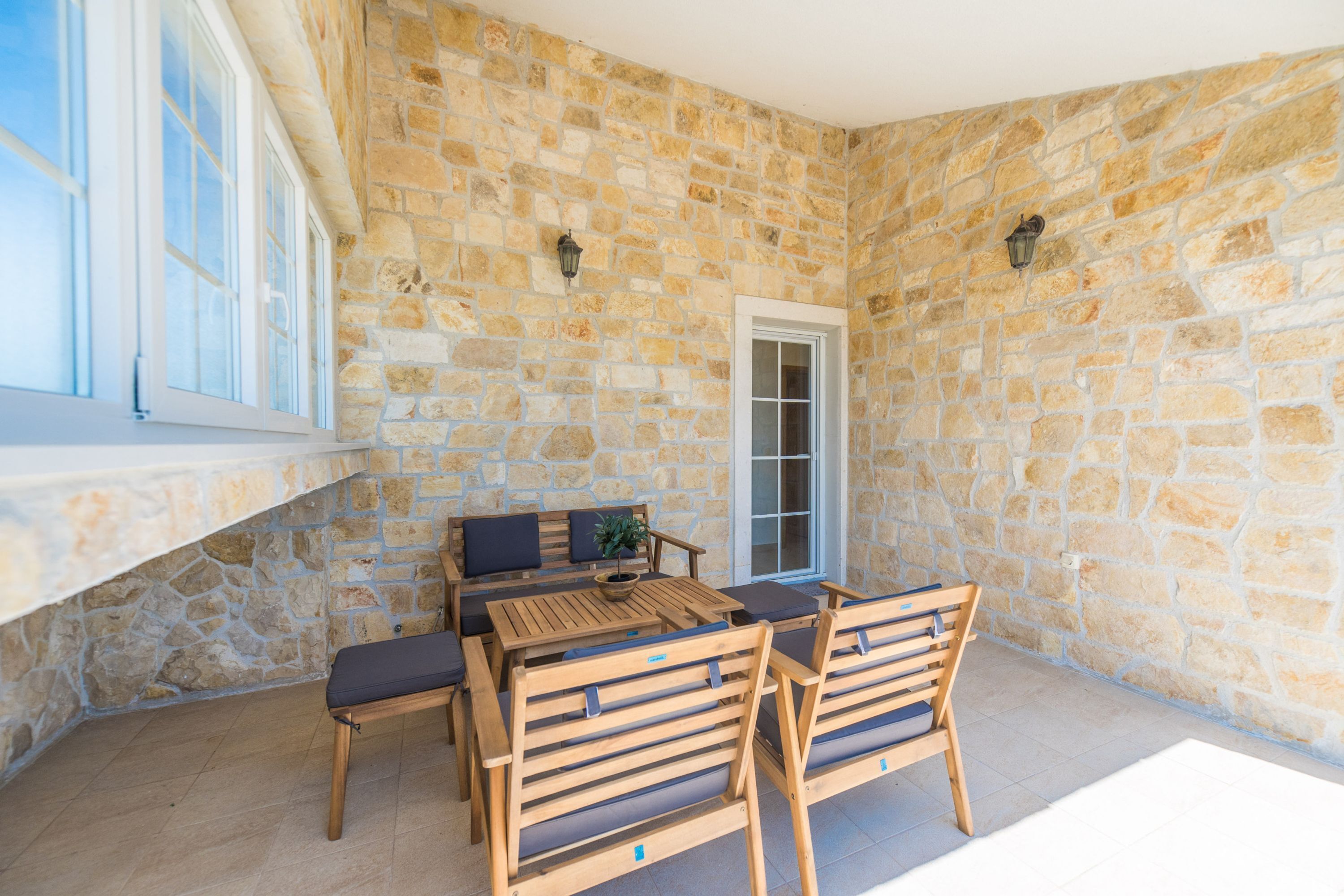 Un patio con paredes de piedra, una mesa y sillas de madera, un banco y una puerta.
