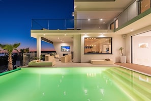 Ett modernt hus med en swimmingpool, en uteplats och ett stort fönster med utsikt över landskapet.