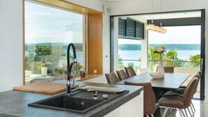 Ett modernt kök med en stor köksö, en matplats med utsikt över havet och ett stort fönster med utsikt över landskapet.
