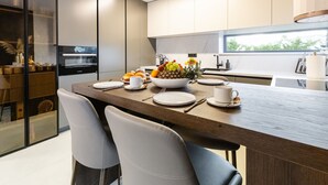 A modern kitchen with a wooden dining table set for four, equipped with a built-in oven and a large bowl of fruit. - Villa Positiva With Heated Pool (Vir)