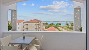 A balcony with a table and chairs, overlooking a coastal view with buildings and a clear sky. - Superior Studio Tania 7 (Sveti Filip i Jakov)