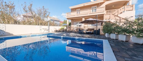 A swimming pool with a clear blue water surface, surrounded by a stone wall and potted plants.