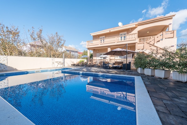 A swimming pool with a clear blue water surface, surrounded by a stone wall and potted plants. - Holiday Home Lolita With Pool (Bibinje)