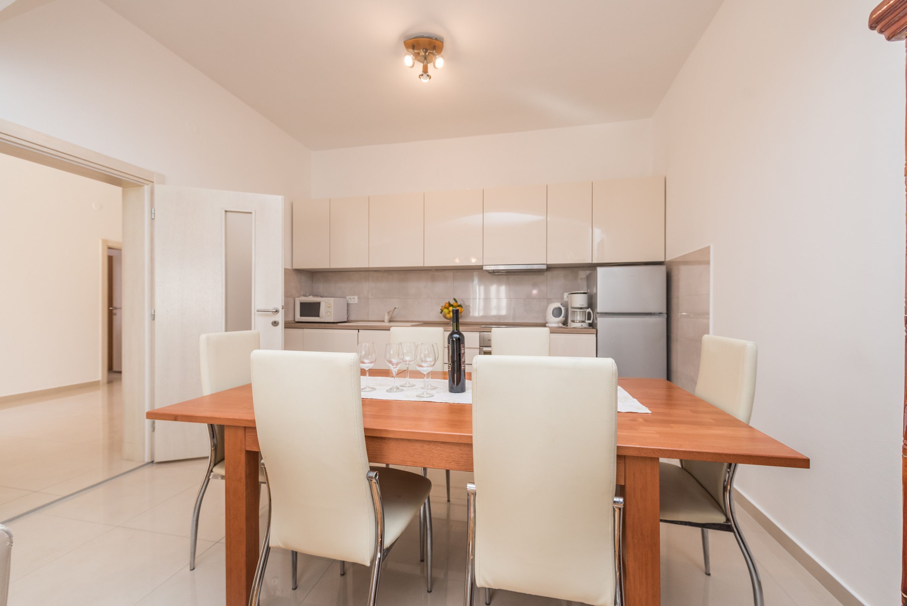 A modern kitchen with white cabinets, a wooden dining table, and four chairs.