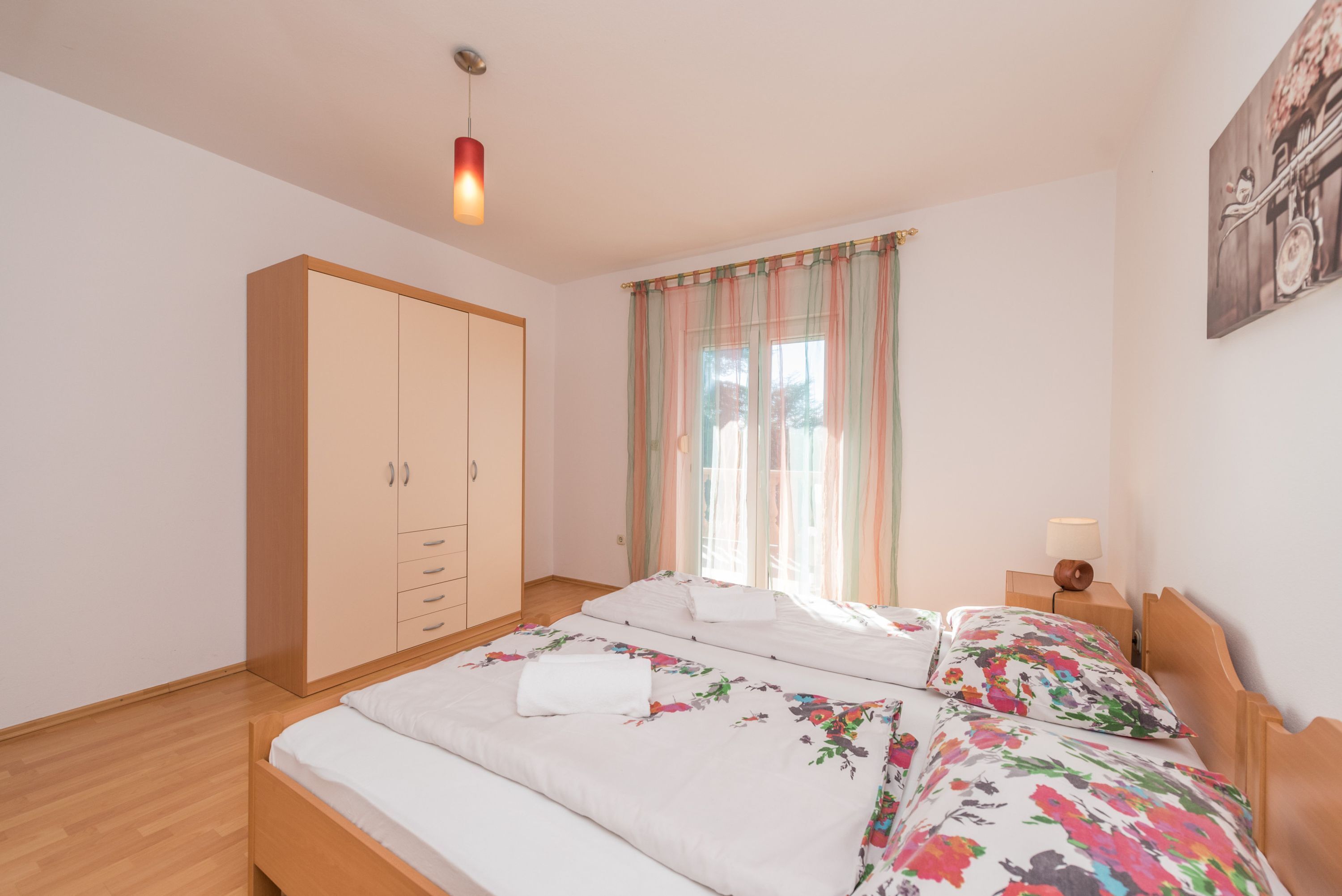 A bedroom with two beds, a wardrobe, a window with curtains, and a painting on the wall.