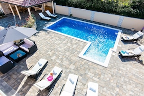 A rectangular swimming pool with a tiled deck, surrounded by lounge chairs and a sun umbrella. - Holiday Home Lolita With Pool (Bibinje)