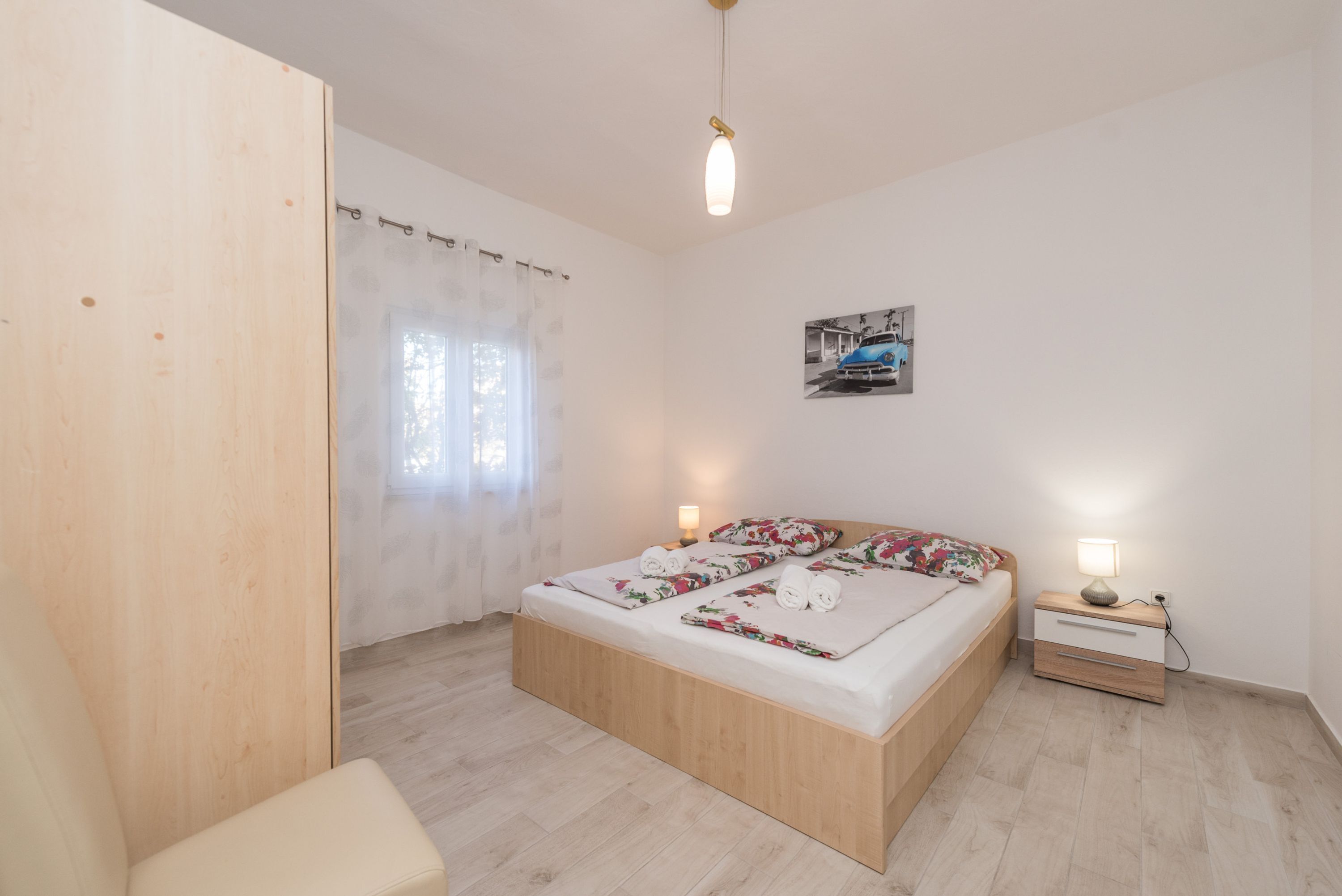 Une chambre à coucher avec un lit en bois, une table de chevet avec une lampe et une fenêtre ornée de rideaux légers.