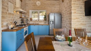 Eine Küche mit blauen Schränken, einem Holzespeisetisch mit Stühlen, einem Kühlschrank und einer Uhr an der Wand.