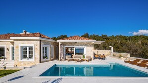 Ein modernes Haus mit Swimmingpool, Naturstein-Fassade und einer Terrasse mit Gartenmöbeln.
