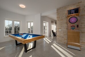 Ein Billardtisch mit Dartscheibe in einem gut beleuchteten Raum mit großen Fenstern und einer Steinsäule.