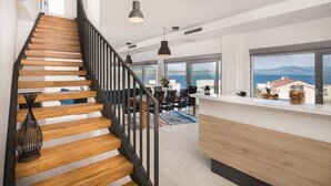 Ein modernes Interieur mit einer Holztreppe, einem Essbereich und großen Fenstern mit Meerblick.