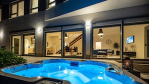 Ein Whirlpool vor einem modernen Haus mit großen Fenstern, einer Treppe und einem sichtbaren Wohnzimmer.