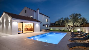 Ein modernes Haus mit Swimmingpool, Sitzgelegenheiten im Freien und einer gut beleuchteten Terrassenfläche.
