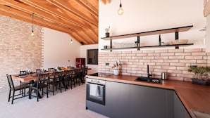 Eine moderne Küche mit Backsteinwand, Holzbalkendecke und einer zentralen Kochinsel mit eingebautem Ofen.