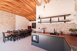 A modern kitchen with a brick wall, wooden ceiling beams, and a central island with a built-in oven. - Villa Elaia With Heated Pool (Sukosan)