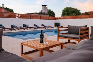 Ein Poolbereich mit Liegestühlen, einem Holztisch mit Flasche und Glas sowie einem Fernsehbildschirm.