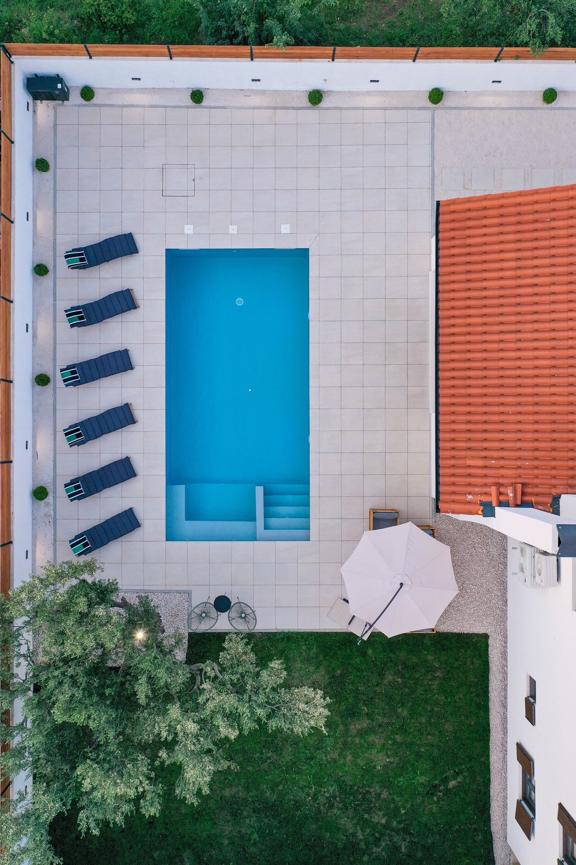 An aerial view of a swimming pool area with lounge chairs, a small table with an umbrella, and a grassy area.