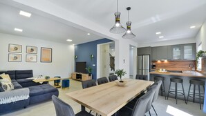 A modern living room with a sofa, dining table, and chairs. There is a kitchen area with a counter and stools. - Villa Rea 3 With Heated Pool (Privlaka)