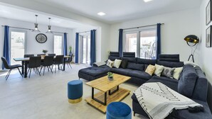 A modern living room with a sectional sofa, a wooden coffee table, and a dining area with a table and chairs. - Villa Rea 3 With Heated Pool (Privlaka)