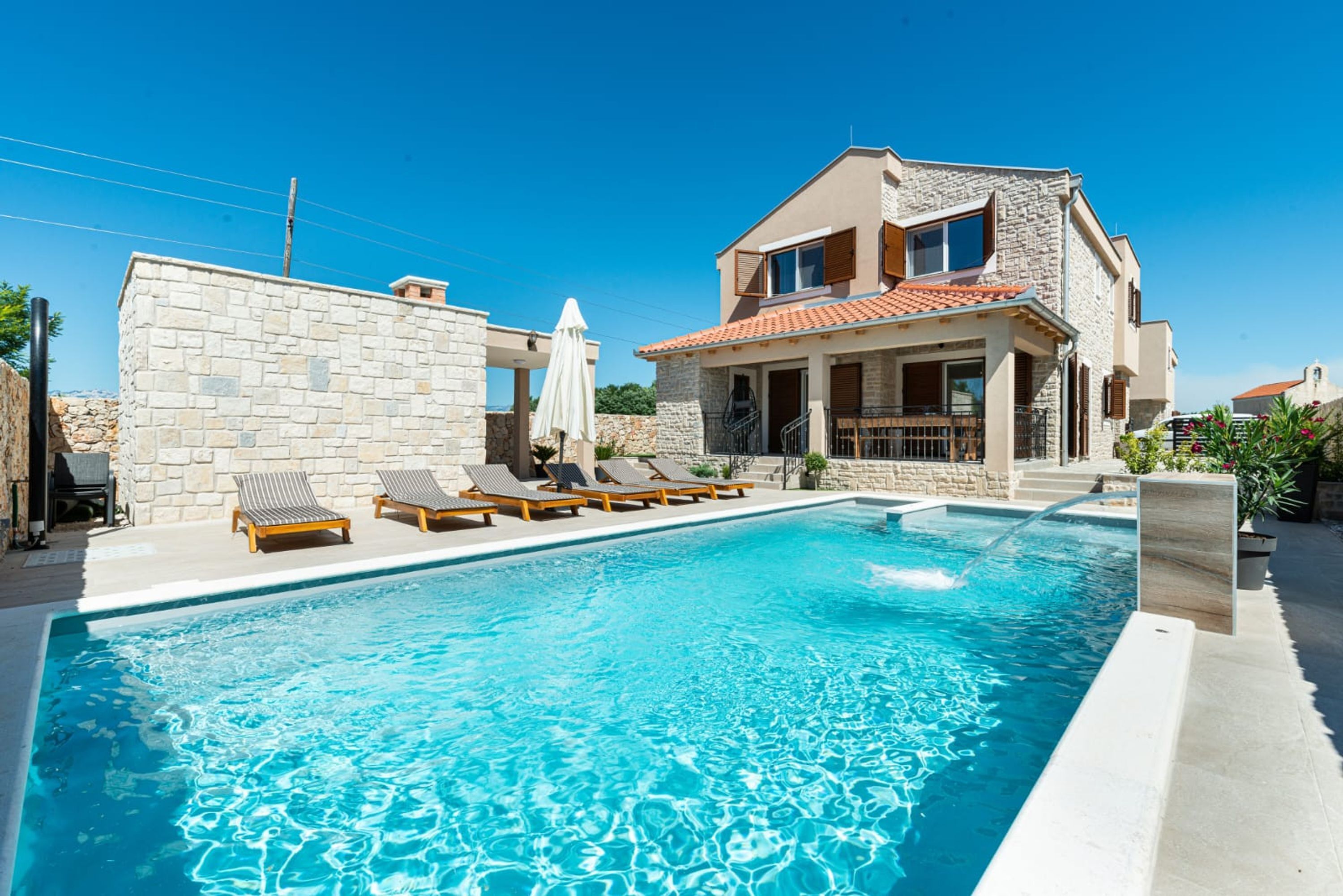 A swimming pool with lounge chairs and a stone wall.