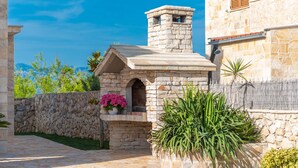 A stone building with a chimney, a stone wall, and a paved area with potted plants. - Villa Edena With Heated Pool (Privlaka)