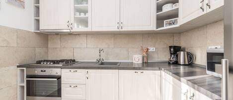 A modern kitchen with white cabinetry, a built-in oven, a gas stove, and a coffee maker.