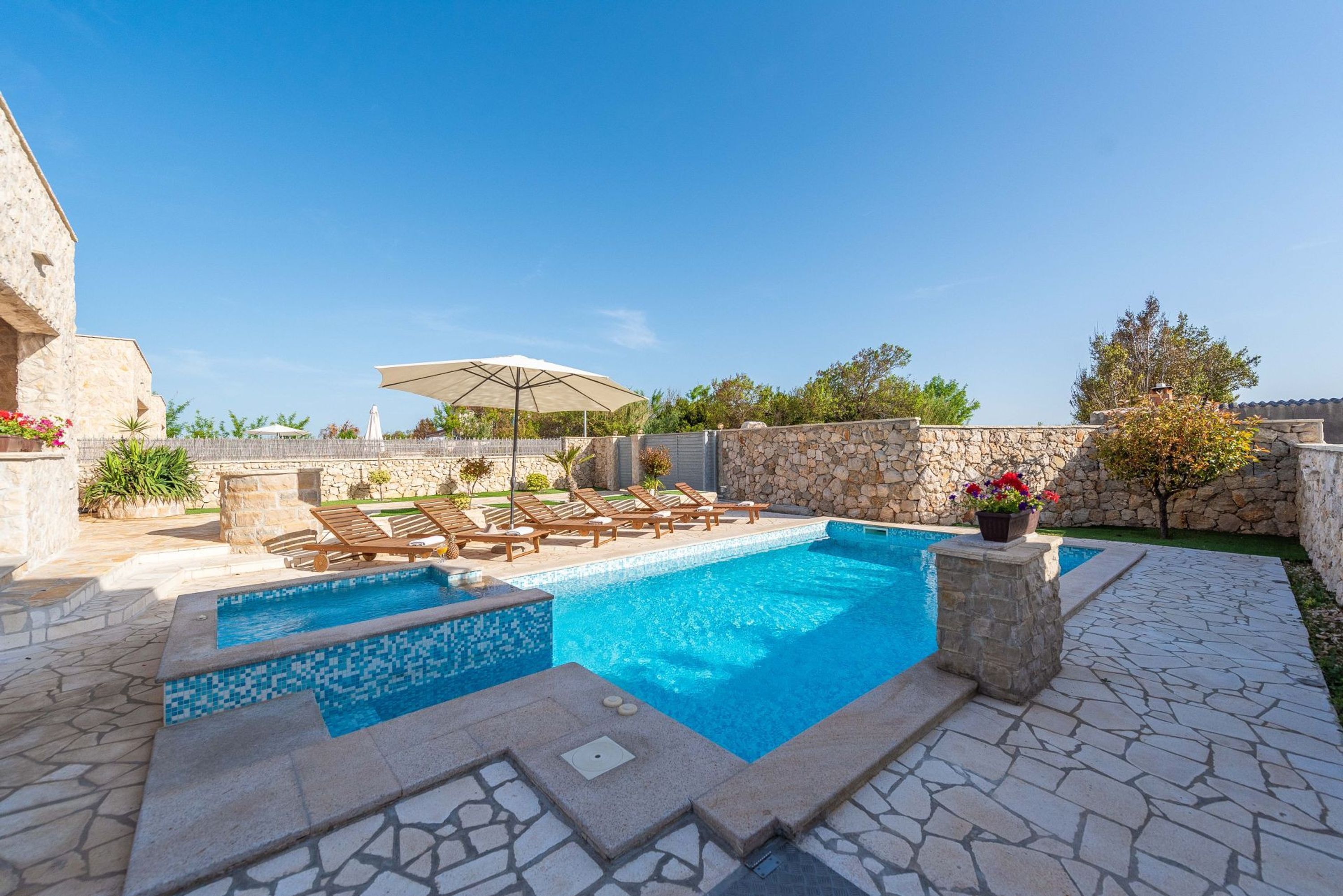A swimming pool with lounge chairs and a stone wall.
